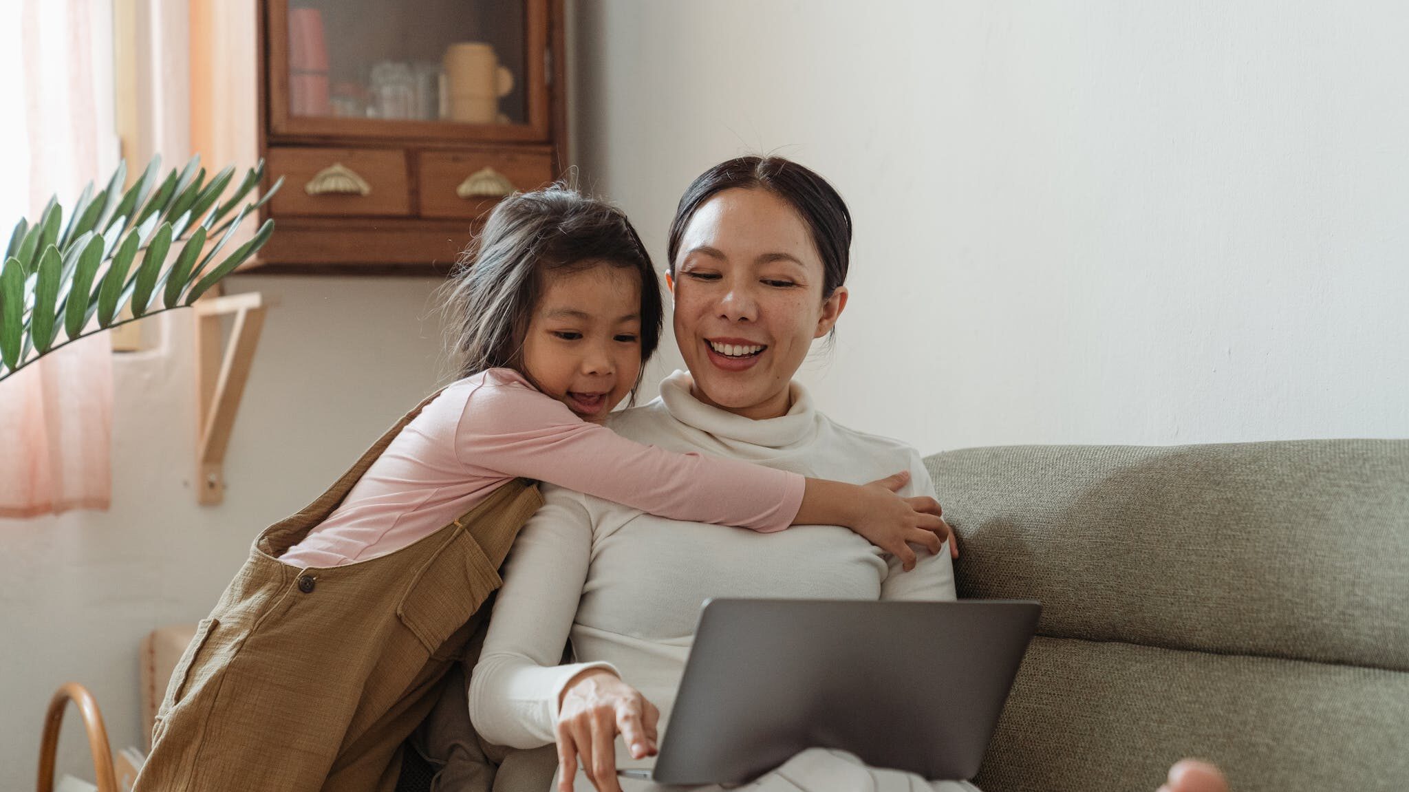 Cheerful girl hugging mother with laptop